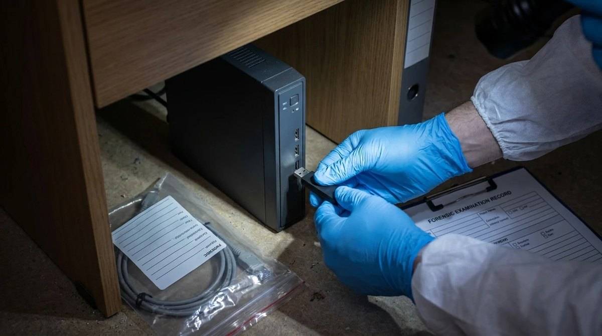 Técnico con guantes extrayendo el video de un grabador de seguridad junto al acta y la bolsa de evidencia (recreación)